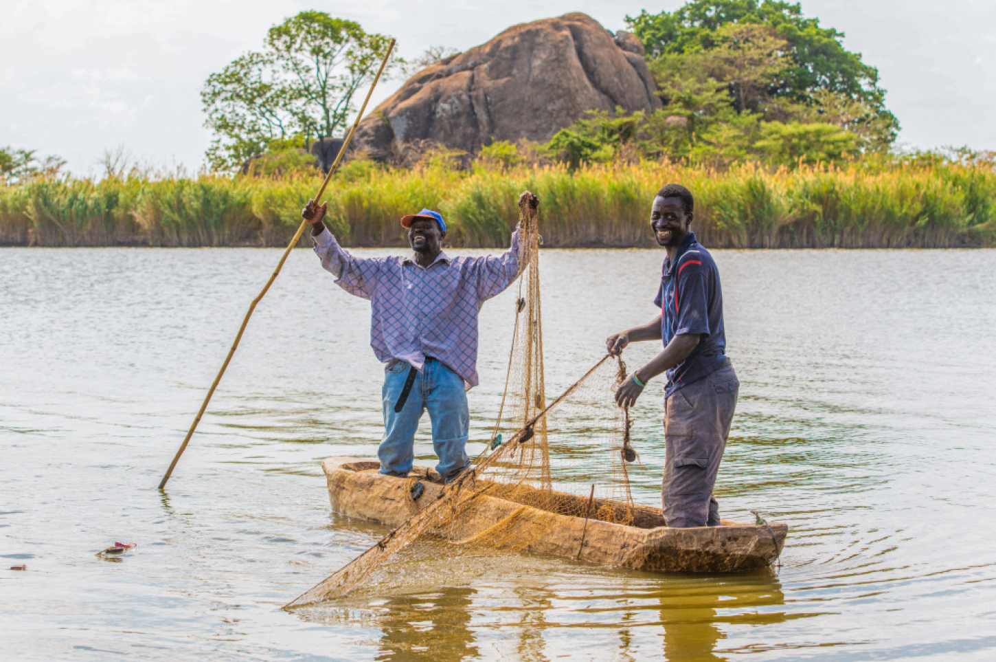 Two small-scale artisanal fishermen proudly standing on their boat in a dam-lake and lifting up their fishing net.