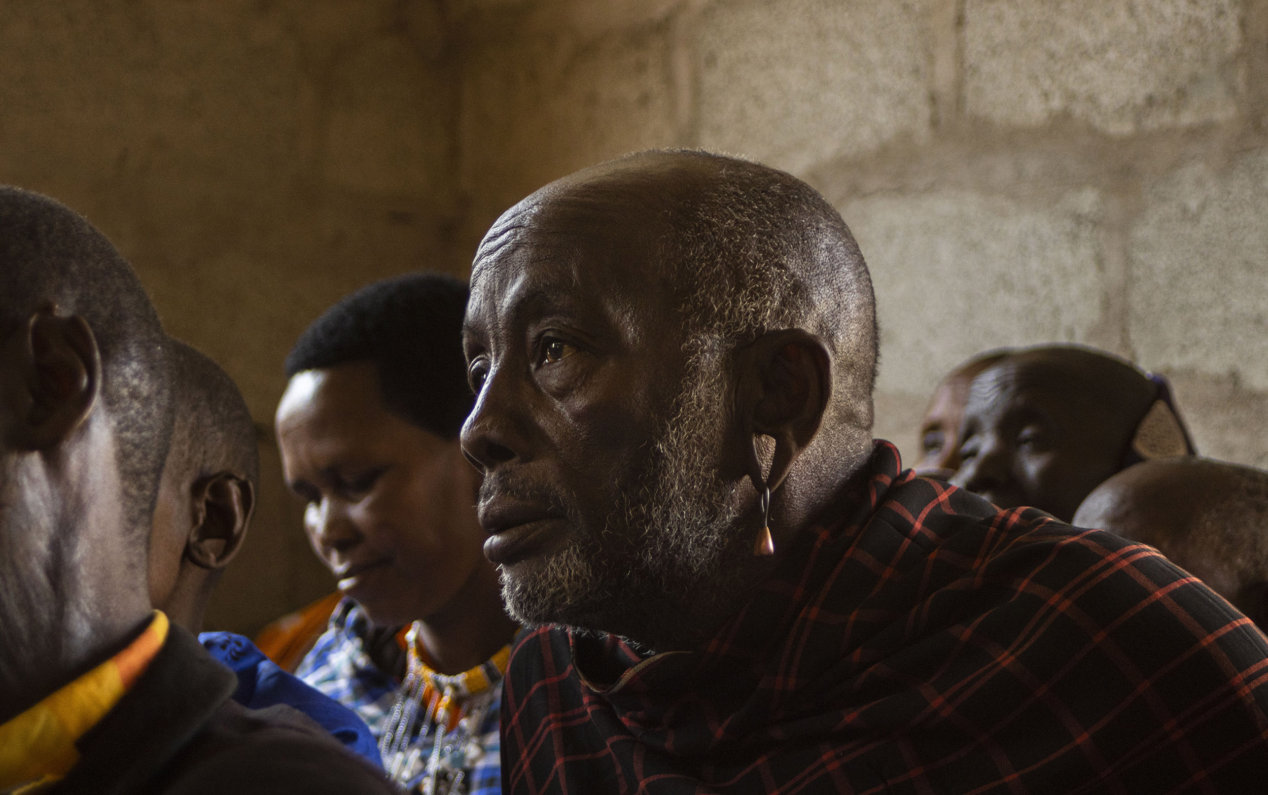 Maasai man sits in a community hall with other local people