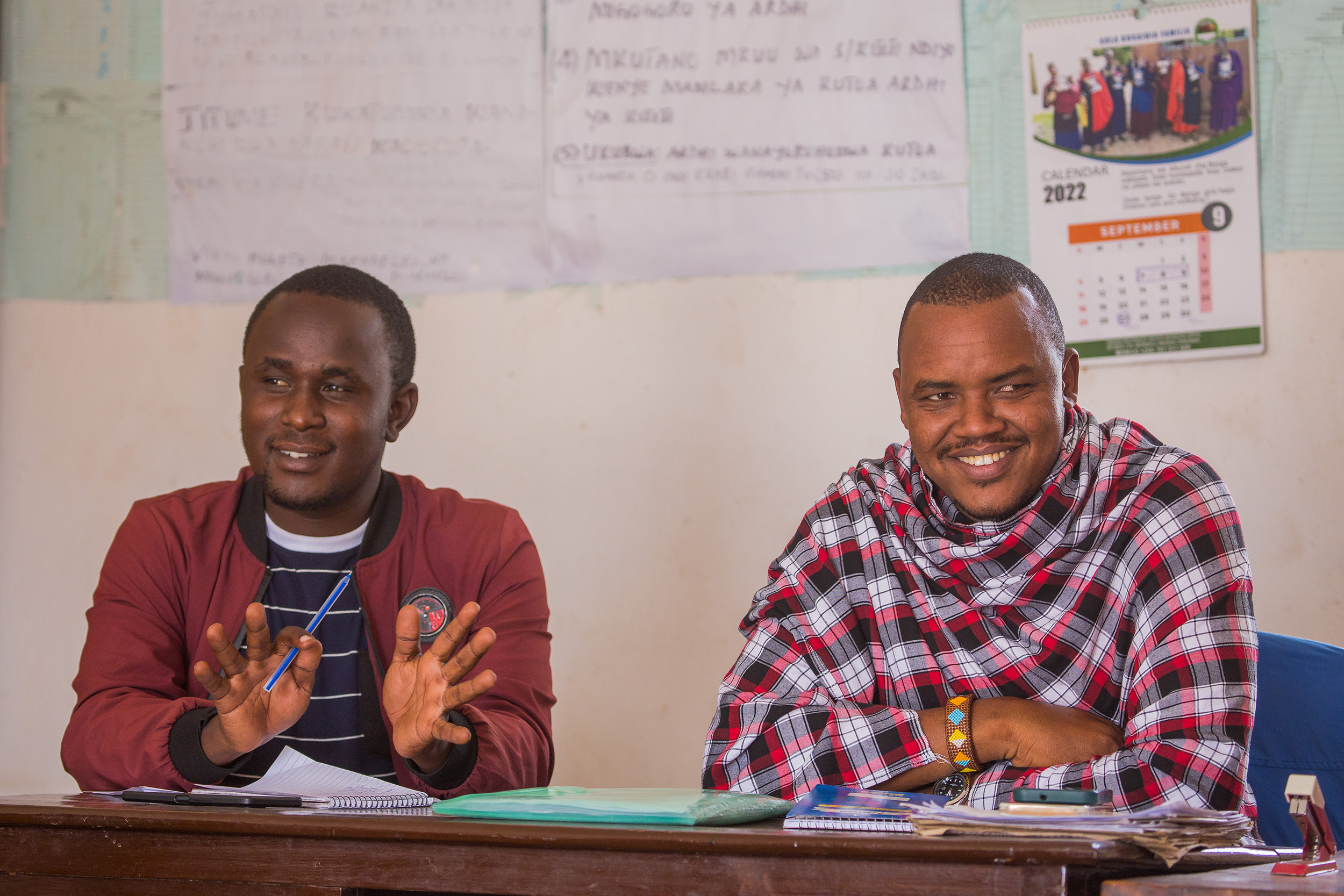 Two young men sit at a desk with smiles in a community hall