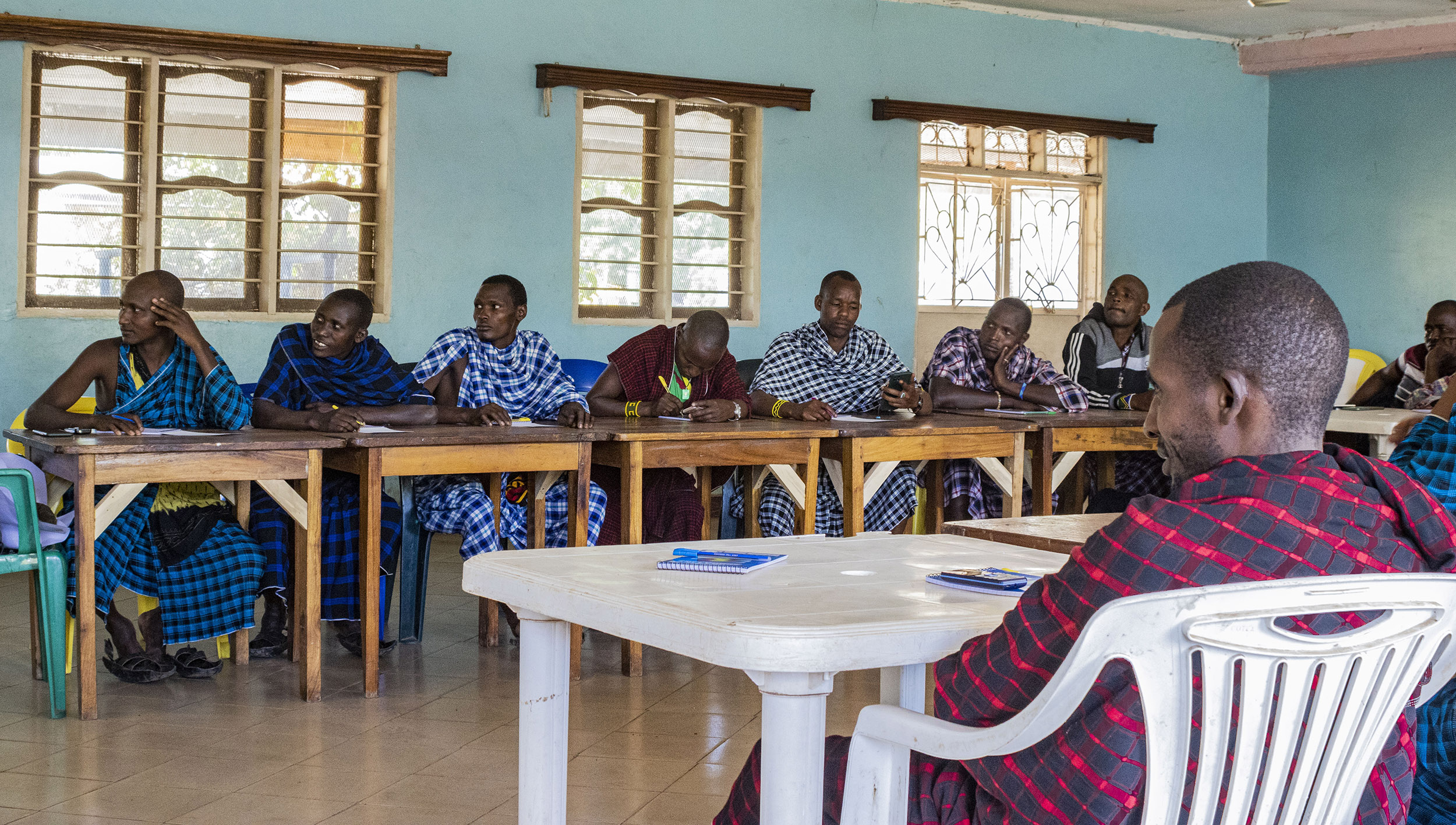 Maasai men sit around tables looking at a speaker