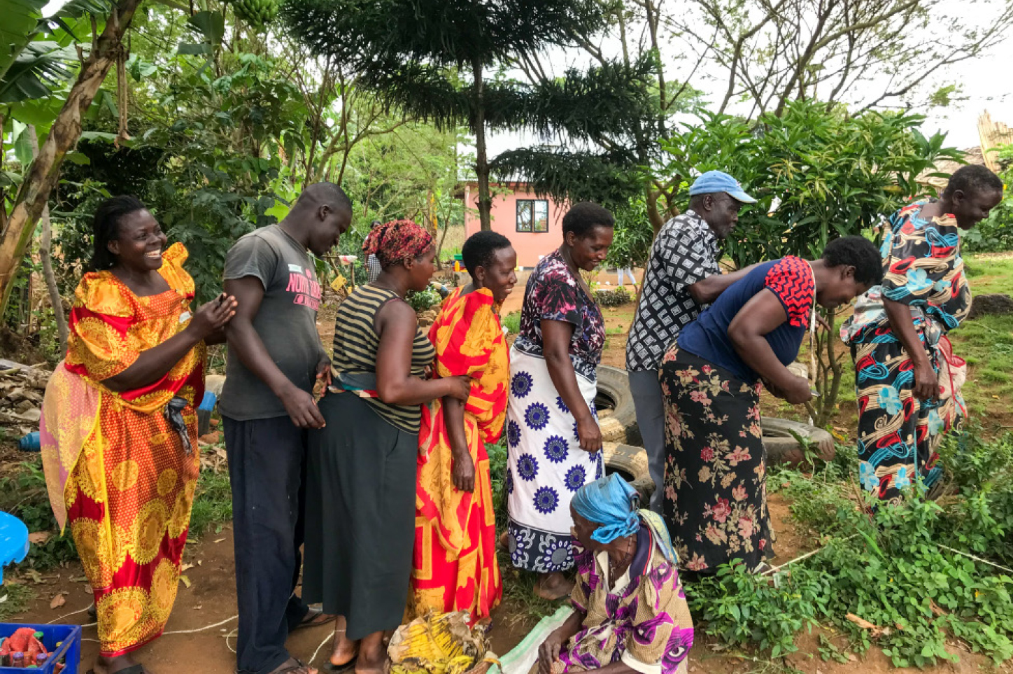 A group of nine people, mainly women, standing and sitting in a row and doing different tasks on the ground. 