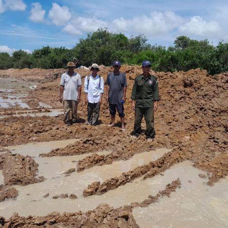 Four Cambodians standing in an excavated fish conservation pond.