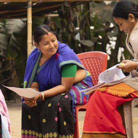 Three women sitting on chairs outside, exchanging while holding planning documents in their hands.