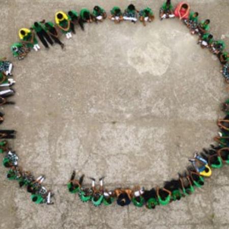 An aerial image of students sitting in a circle on gray pavement.