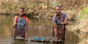 Family showing their successful fish harvest through using the fish trap in a pond.