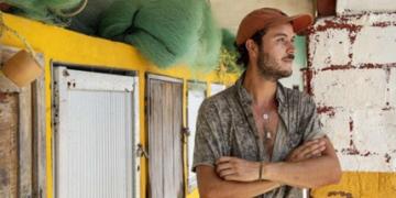 A photo of a extern Juan Suescun as he leans against a pillar. There is fishing gear and nets in the background. 