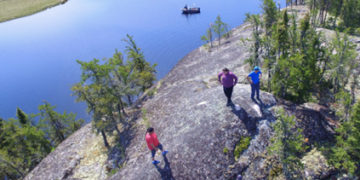 An aerial image of students in Kinosao Sipi, Manitoba. The students are climbing on a rock and a river can be seen in the distance. 