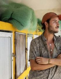 A photo of a extern Juan Suescun as he leans against a pillar. There is fishing gear and nets in the background. 