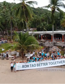 The picture shows a group of participants at a beach holding the "Koh Tao Better Together" campaign sign 